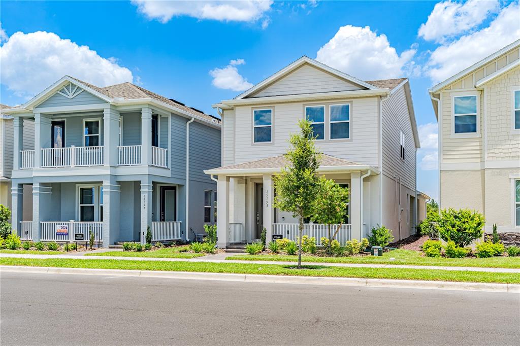 Two suburban houses stand side-by-side with front porches, white railings, and manicured green lawns — 15153 SUMMER HARVEST STREET, WINTER GARDEN, FL