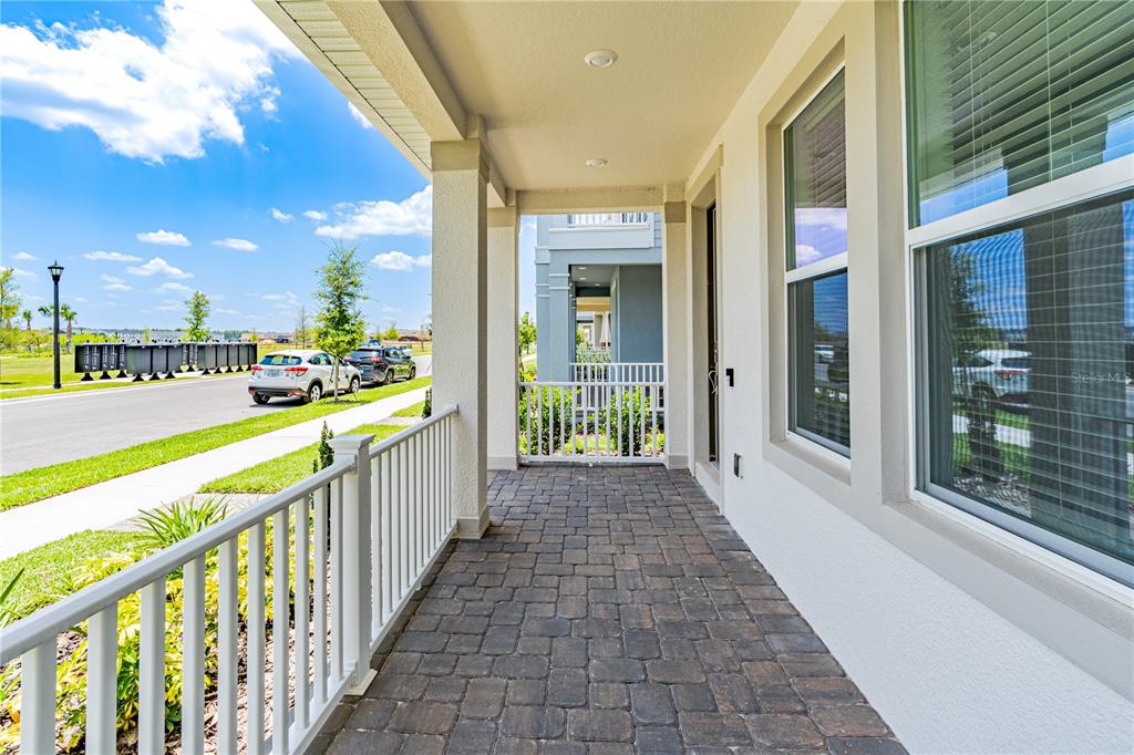 A covered porch with stone pavers, white railings, and a view of a neighborhood street — 15153 SUMMER HARVEST STREET, WINTER GARDEN, FL