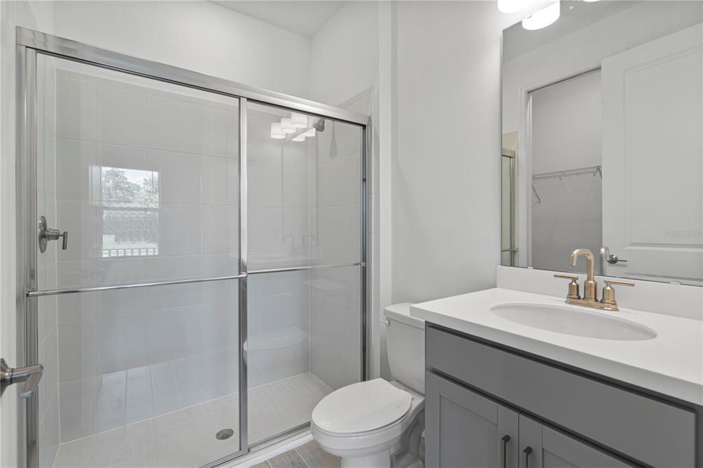 A bathroom features a glass-enclosed shower, a white vanity with a sink, and a toilet — 15153 SUMMER HARVEST STREET, WINTER GARDEN, FL