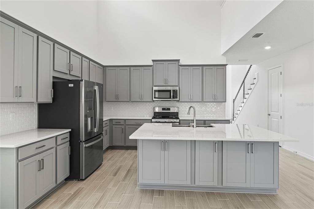 A modern kitchen features gray cabinets, white countertops, stainless steel appliances, and wood-look tile flooring — 15153 SUMMER HARVEST STREET, WINTER GARDEN, FL