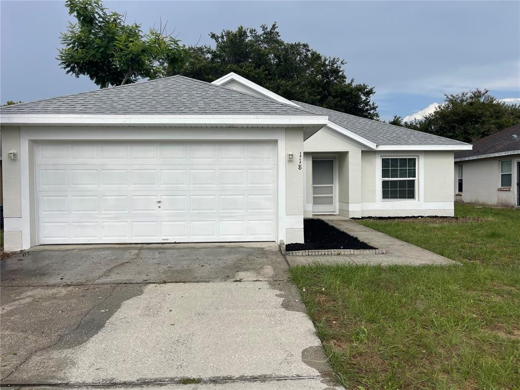 A single-story house with a white garage, light-colored stucco exterior, and a gray shingled roof — 118 SPRINGFIELD PASS, DAVENPORT, FL