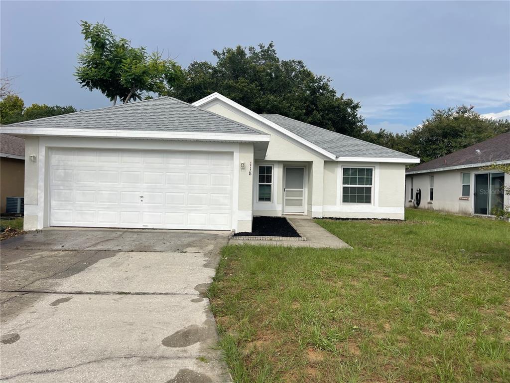 A single-story house with a white garage, light-colored stucco exterior, and a gray shingled roof — 118 SPRINGFIELD PASS, DAVENPORT, FL
