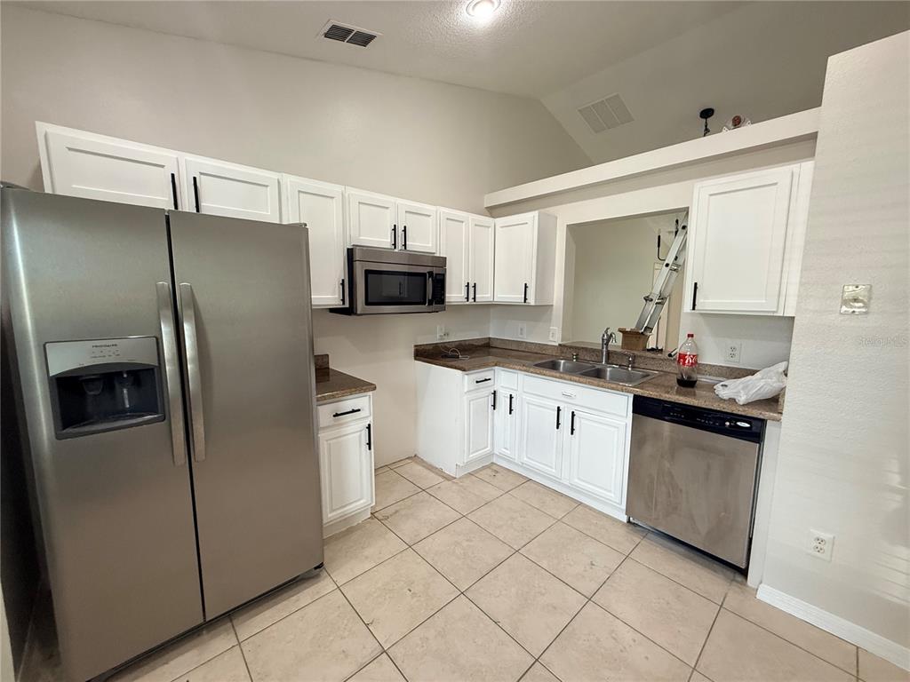 A kitchen features white cabinets, stainless steel appliances, granite countertops, and light-colored tile flooring — 118 SPRINGFIELD PASS, DAVENPORT, FL