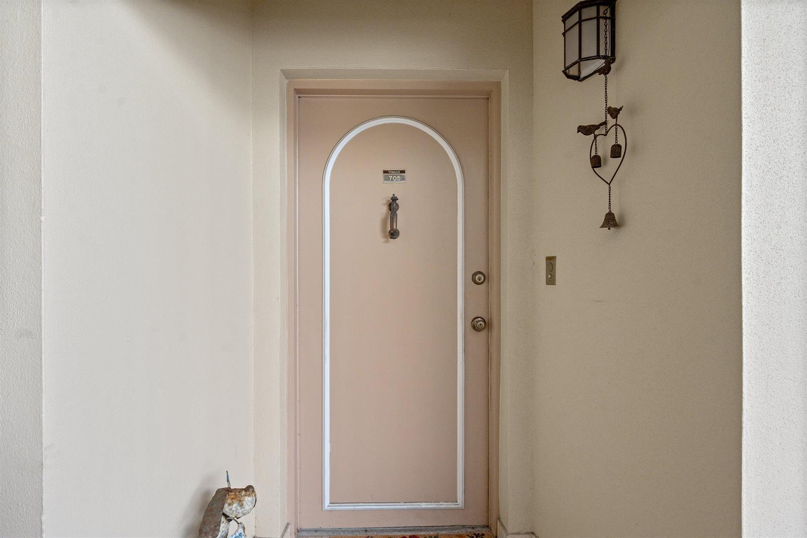A beige arched front door with a brass knocker and a hanging wind chime nearby — 3475 S Ocean Boulevard S Unit 705, Palm Beach FL 33480, PALM BEACH, FL