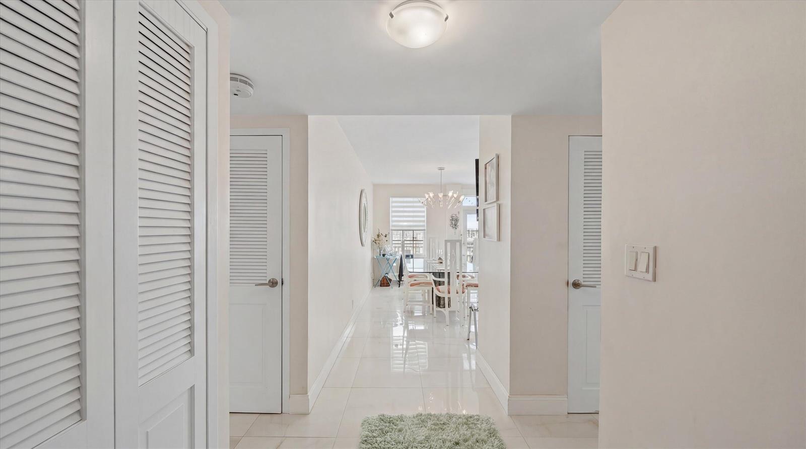 A bright hallway with white tile floors leads toward a dining area with a chandelier — 3475 S Ocean Boulevard S Unit 705, Palm Beach FL 33480, PALM BEACH, FL