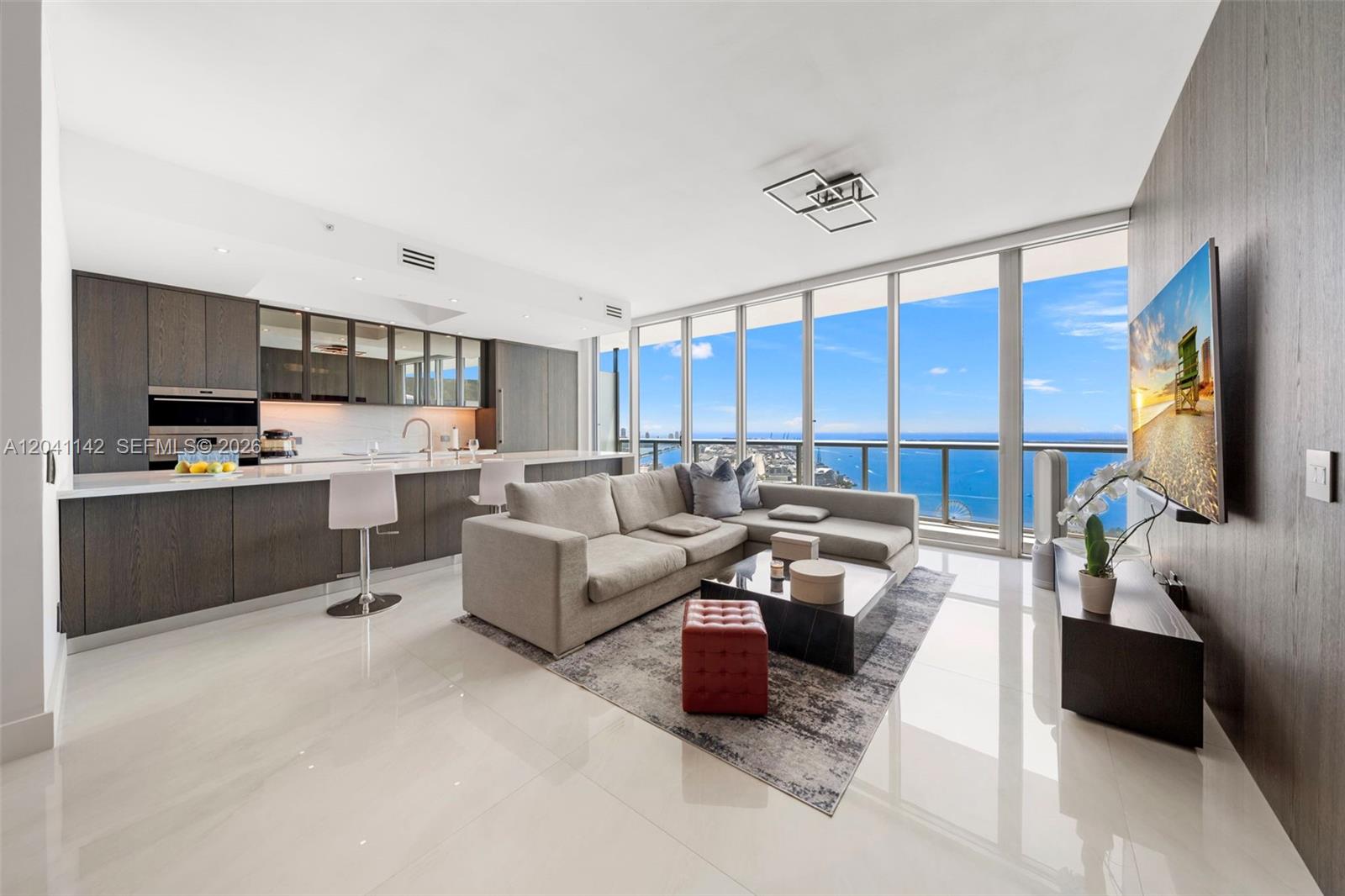 A modern open-concept living room and kitchen feature floor-to-ceiling windows with ocean views — 888 Biscayne Blvd # 5404, Miami FL 33132, MIAMI, FL