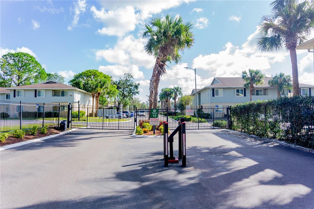 A gated entrance leads to apartment buildings with palm trees under a blue sky — 231 BERRY TREE PLACE, BRANDON, FL
