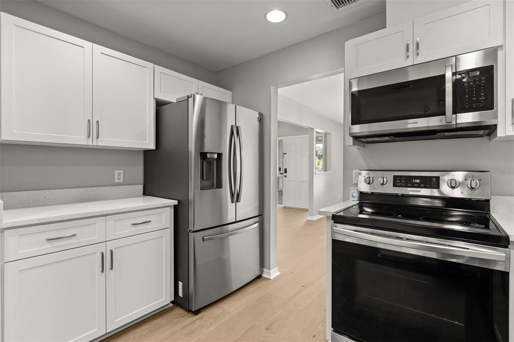 A kitchen with white cabinets, stainless steel appliances, and light wood-look flooring — 925 RED DANDY DRIVE, ORLANDO, FL
