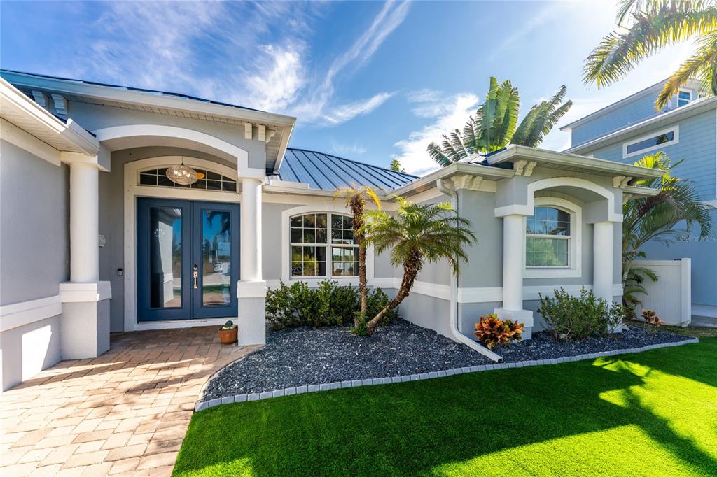 A gray house exterior with a blue front door, metal roof, and artificial grass lawn — 16168 LA BARGE CIRCLE, PORT CHARLOTTE, FL
