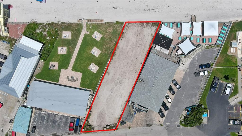 An aerial view shows a vacant rectangular lot situated between two commercial buildings near a beach — 0 BUENOS AIRES AVENUE, NEW SMYRNA BEACH, FL