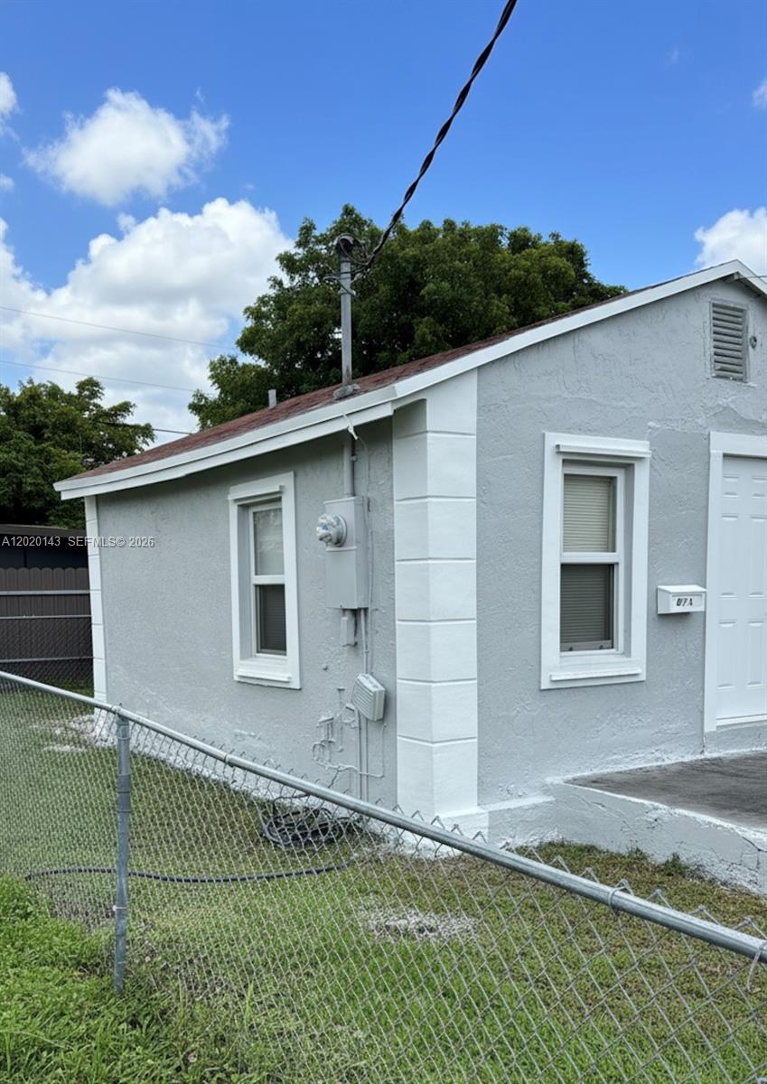 A gray, single-story house exterior features white trim, a chain-link fence, and an electrical meter — 2103 NW 57th St, Miami FL 33142, MIAMI, FL
