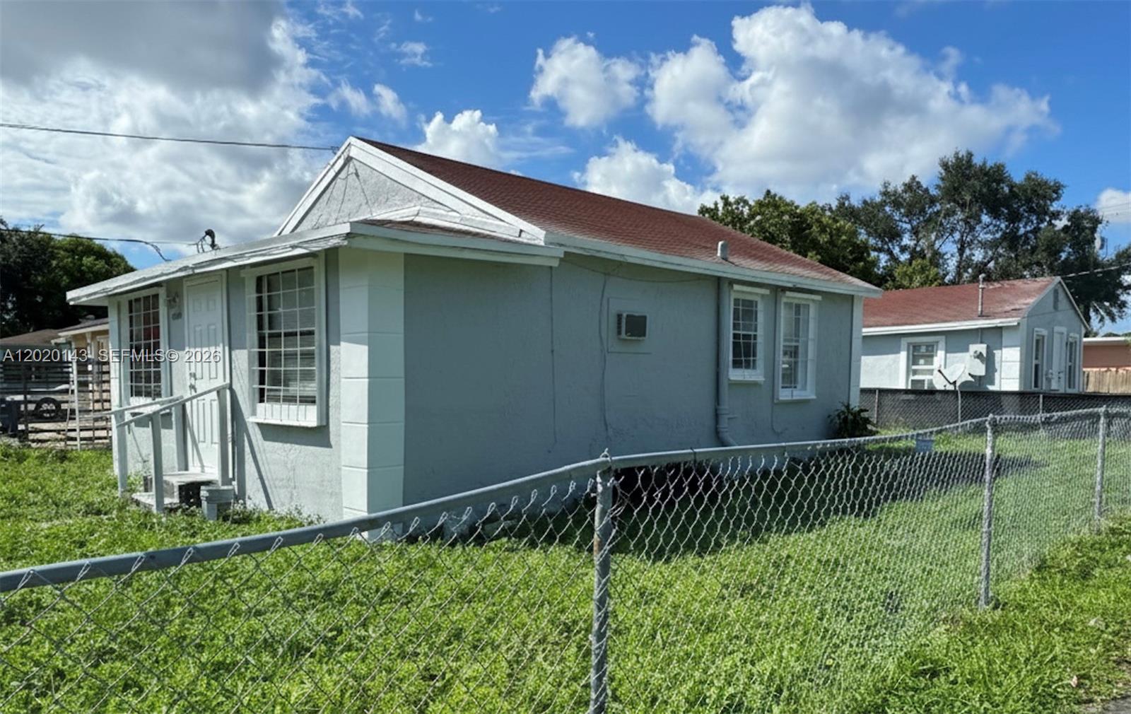 A single-story gray house with a red roof stands behind a chain-link fence — 2103 NW 57th St, Miami FL 33142, MIAMI, FL