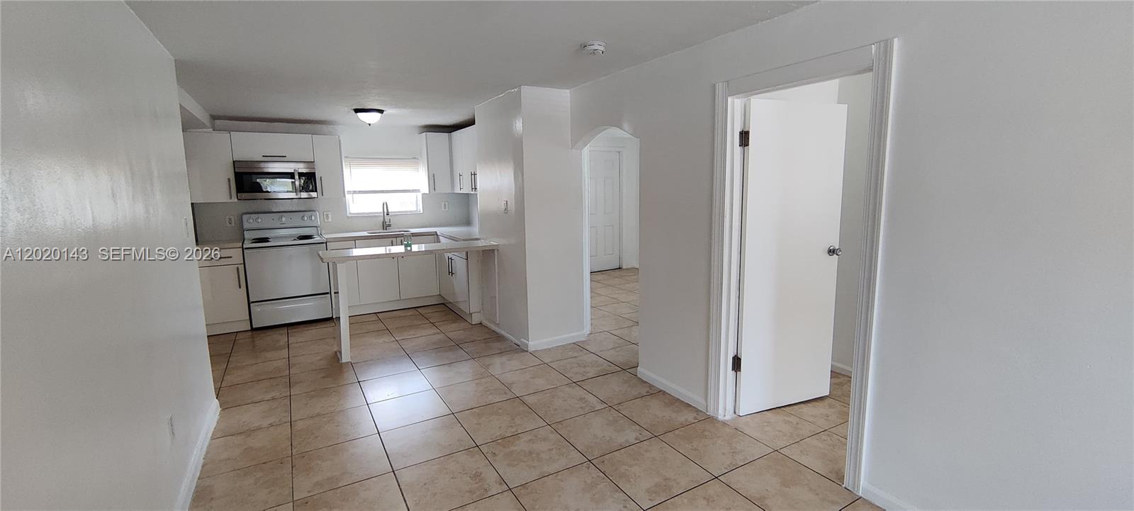 A white kitchen with tile flooring features a breakfast bar and an adjacent doorway — 2103 NW 57th St, Miami FL 33142, MIAMI, FL