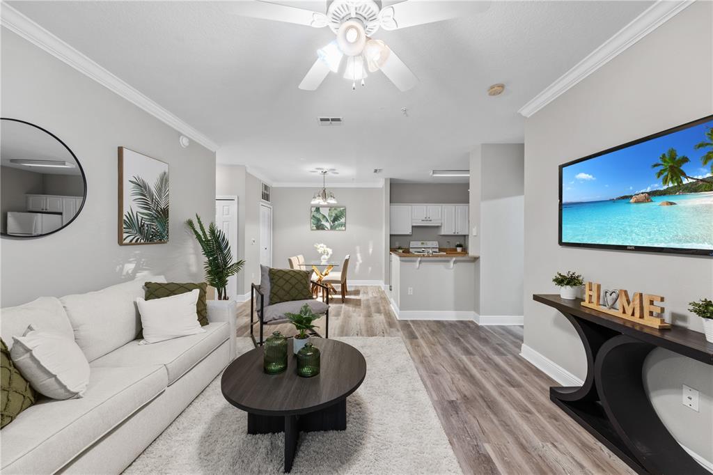 A living room with a white sofa, round coffee table, and wall-mounted television — 130 SOUTHERN PECAN CIRCLE UNIT 103, WINTER GARDEN, FL