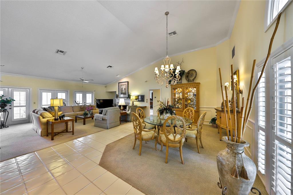 An open-concept living and dining area features vaulted ceilings, tile and carpet flooring, and furniture — 2446 SWEETWATER COUNTRY CLUB DRIVE, APOPKA, FL