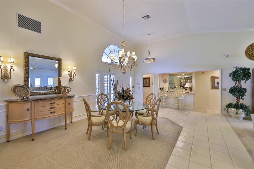 A dining room with a glass table, chandelier, buffet, and tile and carpeted flooring — 2446 SWEETWATER COUNTRY CLUB DRIVE, APOPKA, FL