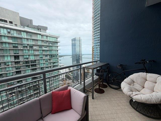 A balcony features a sofa, a high-top table with stools, and a bicycle overlooking city buildings — 60 SW 13th St # 4810, Miami FL 33130, MIAMI, FL