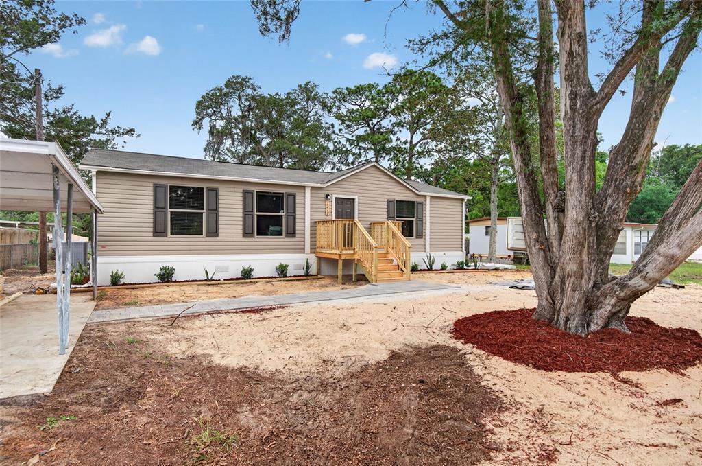 A tan manufactured home with a wooden front porch and a large tree in front — 3219 WELSH STREET, SPRING HILL, FL