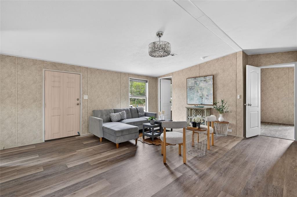 A living room features wood-look flooring, beige paneled walls, a gray sectional sofa, and chairs — 3219 WELSH STREET, SPRING HILL, FL