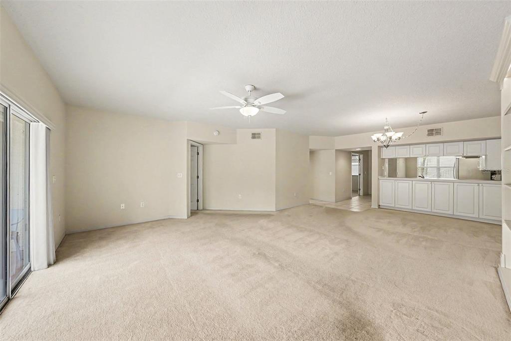 A spacious living room with beige carpet, a ceiling fan, and a white kitchen bar — 1400 WATER VIEW DRIVE W UNIT 102, LARGO, FL