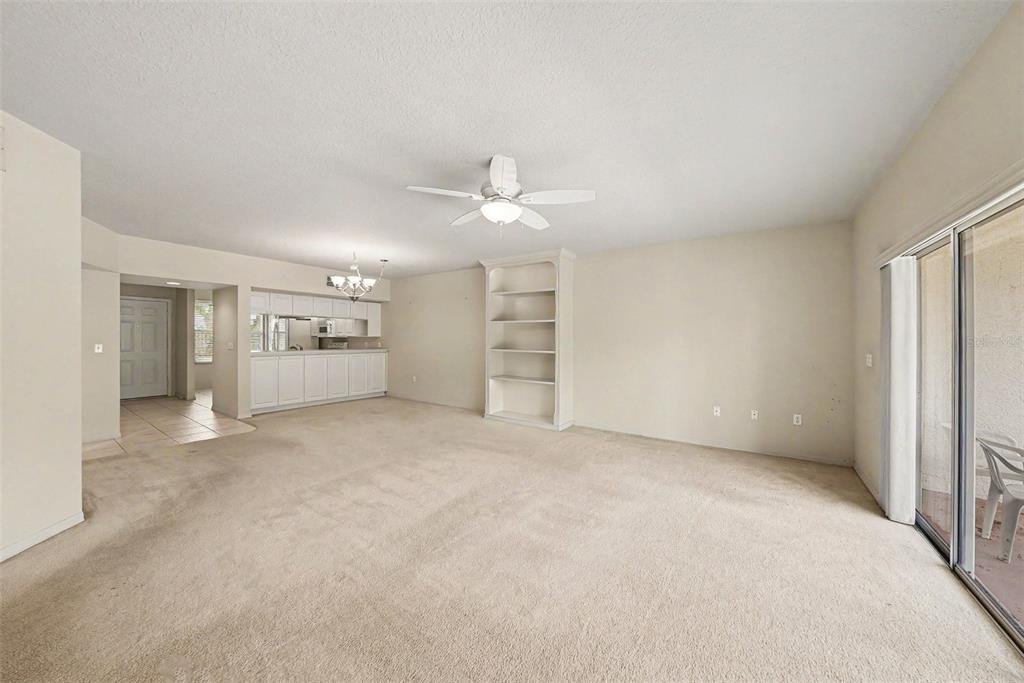 A living room with beige carpet, a ceiling fan, built-in shelving, and sliding glass doors — 1400 WATER VIEW DRIVE W UNIT 102, LARGO, FL