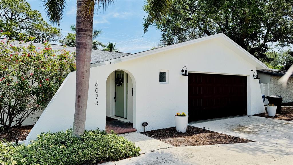 A white house exterior features a dark garage door, an arched entryway, and a palm tree — 6073 TANGLEWOOD DRIVE NE, ST PETERSBURG, FL