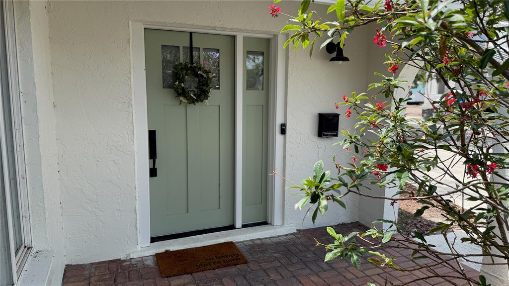 A sage green front door with a wreath and a side light on a porch — 6073 TANGLEWOOD DRIVE NE, ST PETERSBURG, FL