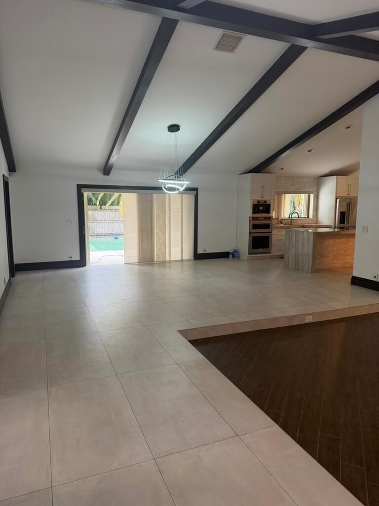 A spacious open-concept living area with vaulted ceilings, dark beams, tile flooring, and a kitchen — 9553 Majestic Way, Boynton Beach FL 33437, BOYNTON BEACH, FL
