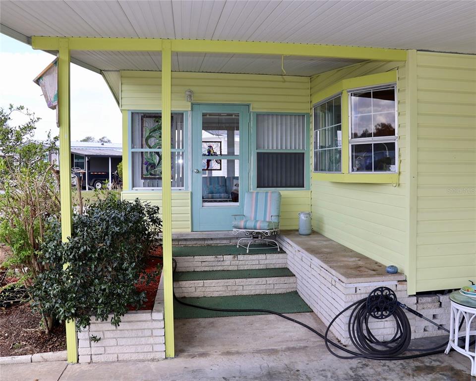 A light green mobile home exterior features a covered porch with brick steps and siding — 1610 REYNOLDS ROAD UNIT 73, LAKELAND, FL