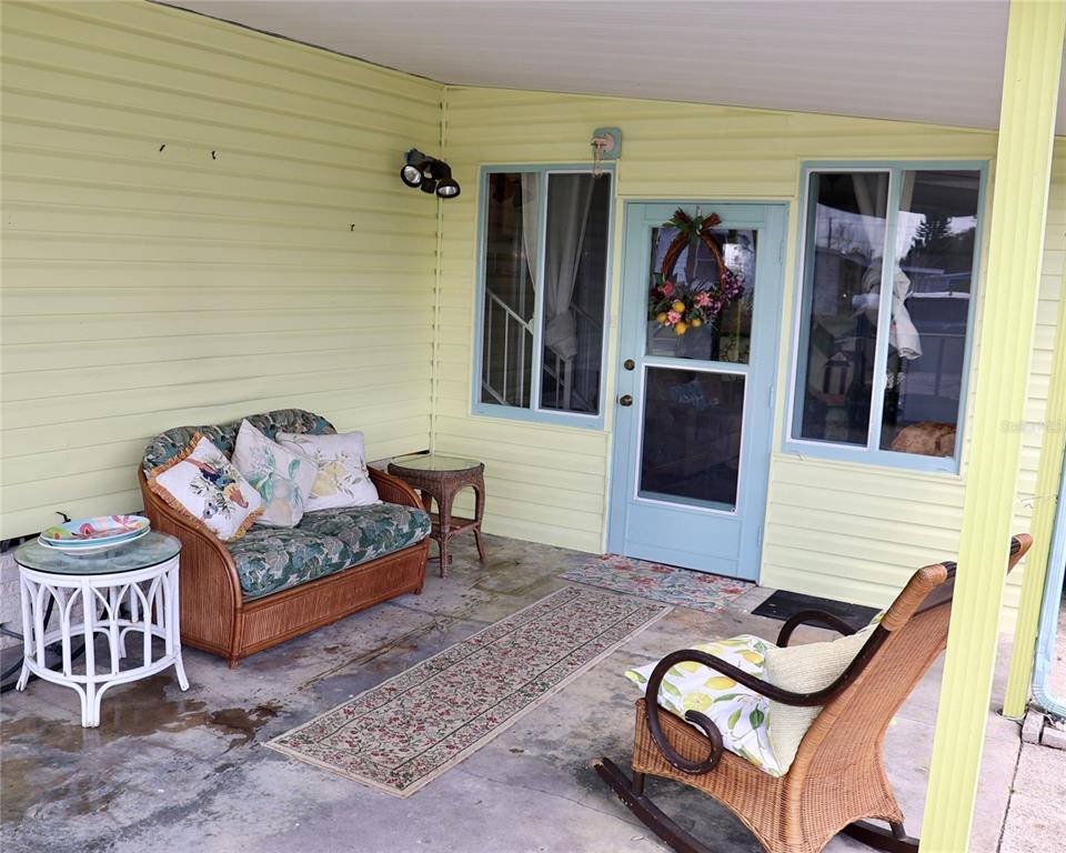 A covered porch features light yellow siding, a blue door, wicker furniture, and concrete flooring — 1610 REYNOLDS ROAD UNIT 73, LAKELAND, FL