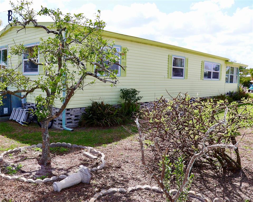 A light yellow mobile home with a tree in the foreground and stone-patterned skirting — 1610 REYNOLDS ROAD UNIT 73, LAKELAND, FL