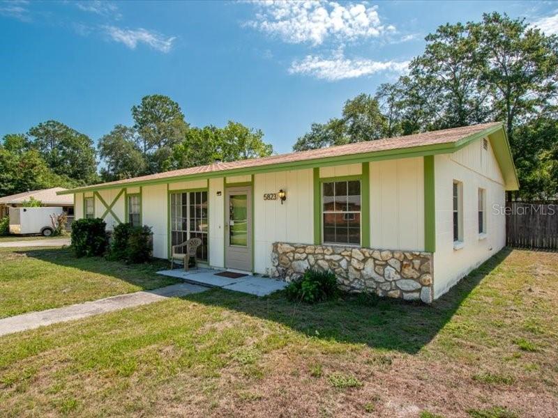 A single-story house with light-colored siding, green trim, and a stone facade base — 5823 NW 26TH STREET, GAINESVILLE, FL