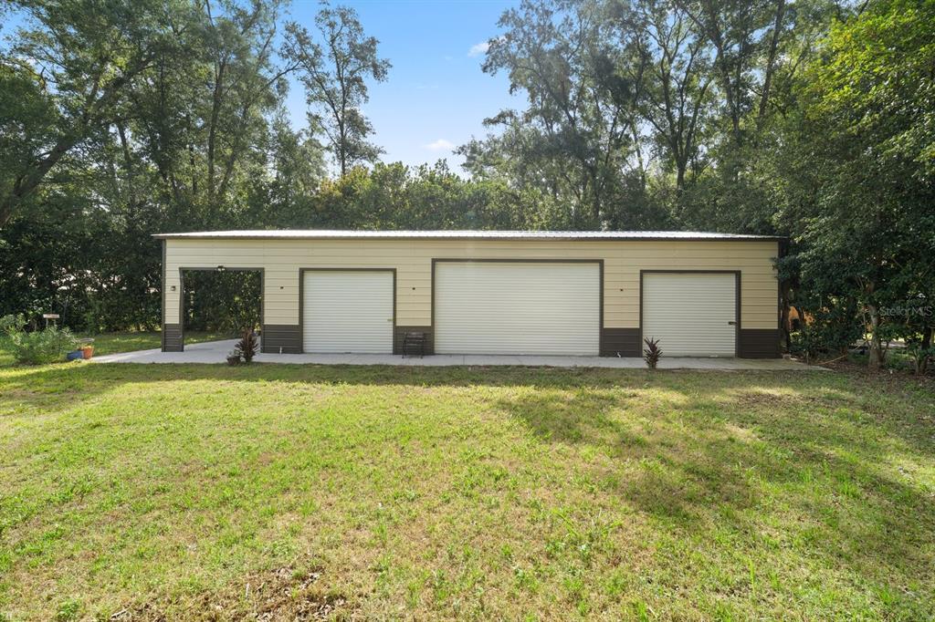 A detached metal garage with three roll-up doors and an open-air bay on the left — 7651 LAKE ANDREA CIRCLE, MOUNT DORA, FL