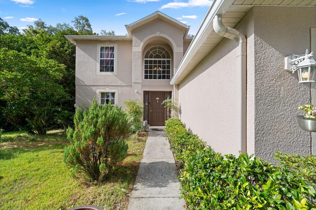 A two-story house with a beige stucco exterior, arched entryway, and a concrete walkway — 7651 LAKE ANDREA CIRCLE, MOUNT DORA, FL