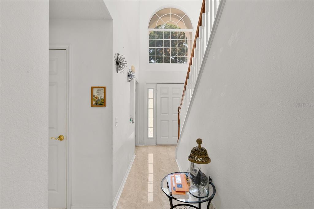 A bright entryway features a staircase, a tall arched window, and a small glass table — 7651 LAKE ANDREA CIRCLE, MOUNT DORA, FL