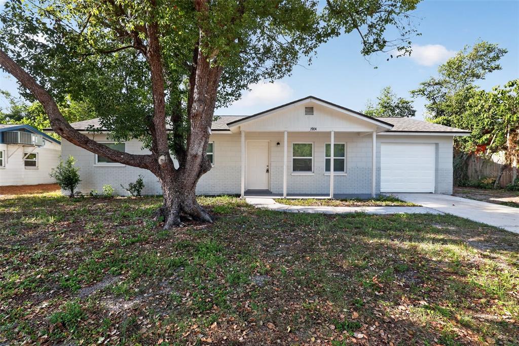 A single-story house with a light-colored brick exterior, a front porch, and a large tree — 1904 E 115TH AVENUE, TAMPA, FL