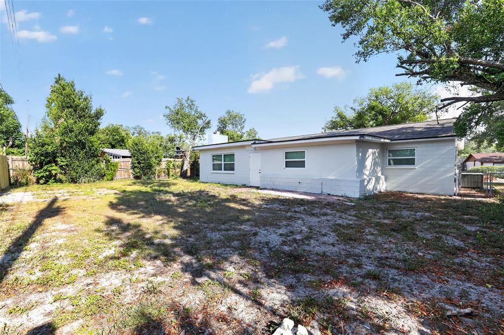 The exterior of a single-story house with a large, sandy backyard and mature trees — 1904 E 115TH AVENUE, TAMPA, FL