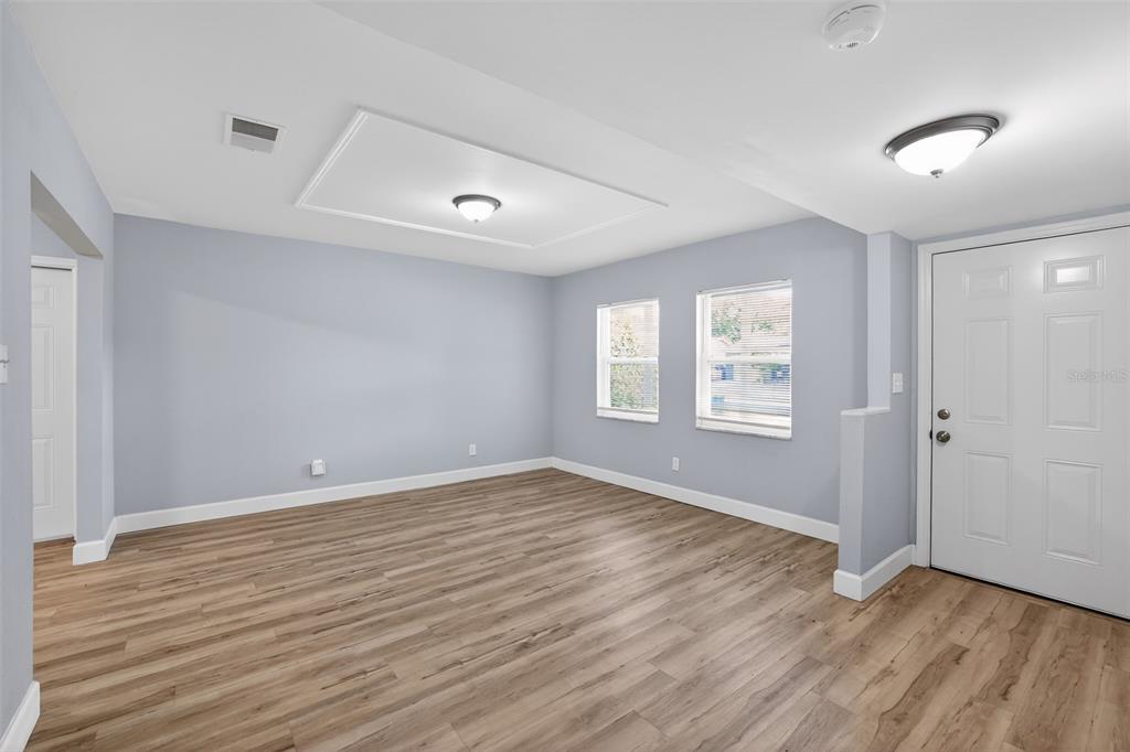 An empty room with light blue walls, wood-look flooring, two windows, and a white door — 1904 E 115TH AVENUE, TAMPA, FL