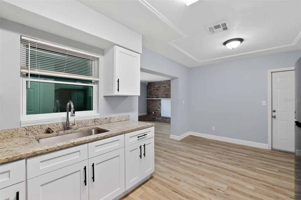 A kitchen with white cabinets, granite countertops, and light wood-look flooring — 1904 E 115TH AVENUE, TAMPA, FL