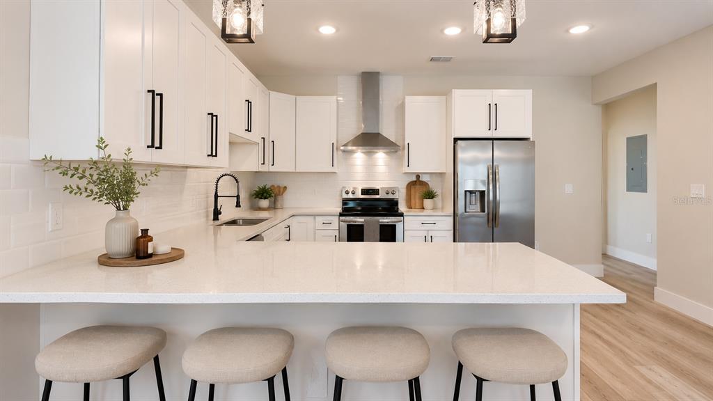 A modern kitchen features white cabinetry, stainless steel appliances, quartz countertops, and four bar stools — 4710 21ST STREET N, ST PETERSBURG, FL