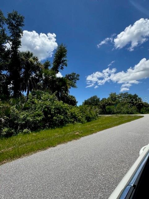 A paved road curves past a grassy lot with dense trees and shrubs under a sky — 14399 MC CLELLAN AVENUE, PORT CHARLOTTE, FL