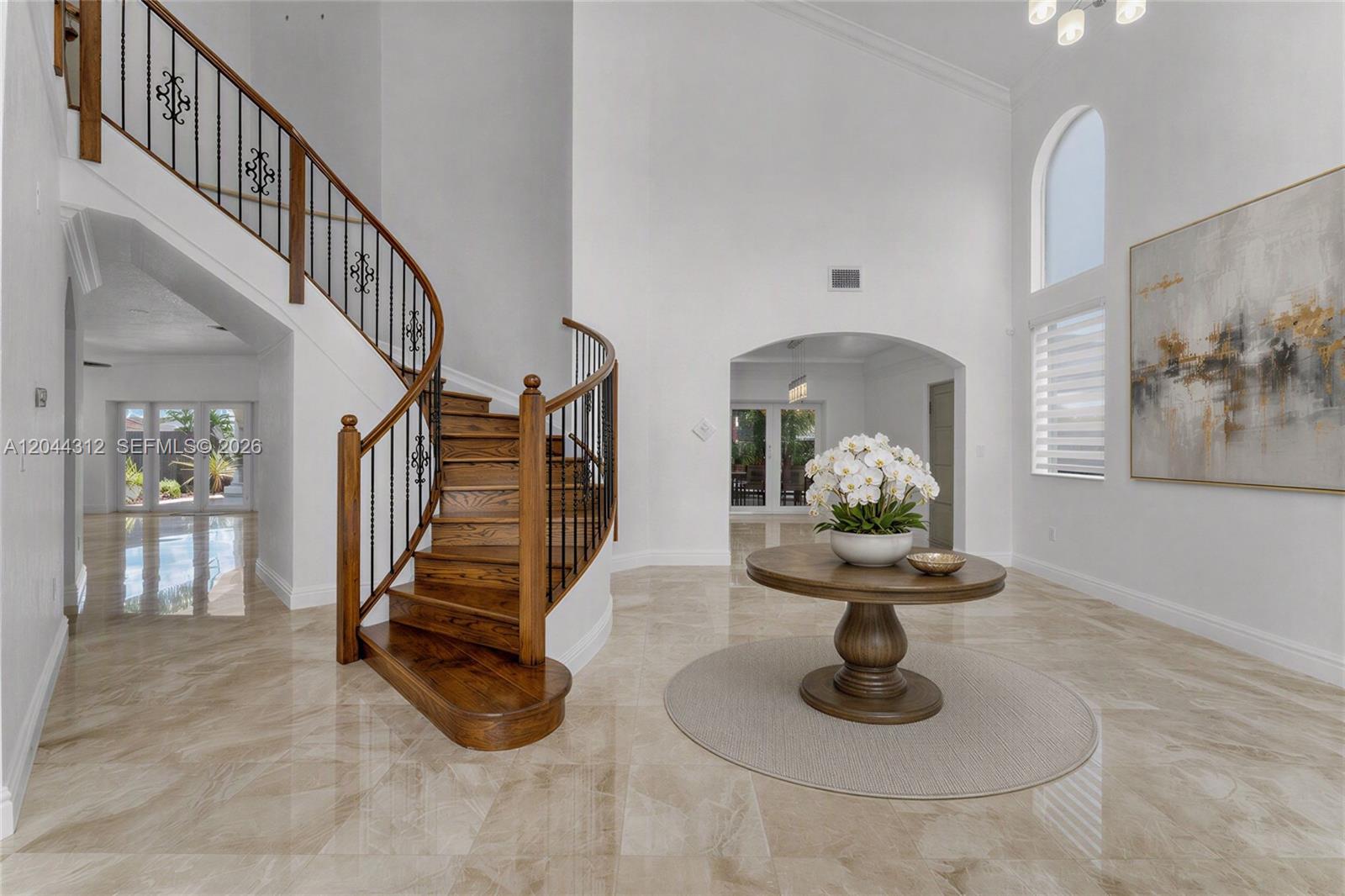 A grand foyer features a curved wooden staircase, marble flooring, and a central pedestal table — 15262 SW 11th St, Miami FL 33194, MIAMI, FL