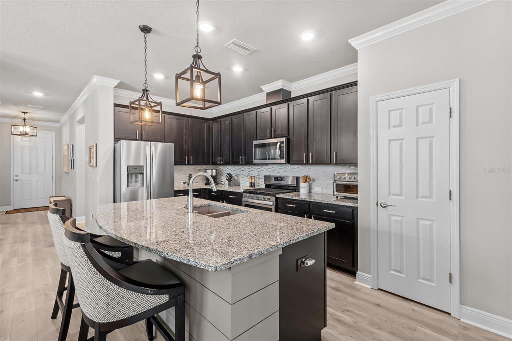 A kitchen features dark wood cabinets, granite countertops, a central island, and stainless steel appliances — 15180 RENAISSANCE AVENUE, ODESSA, FL