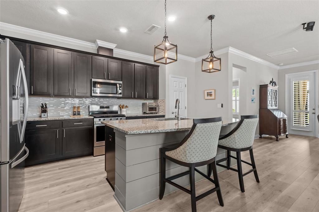 A kitchen with dark cabinets, a gray island with bar seating, and light wood flooring — 15180 RENAISSANCE AVENUE, ODESSA, FL