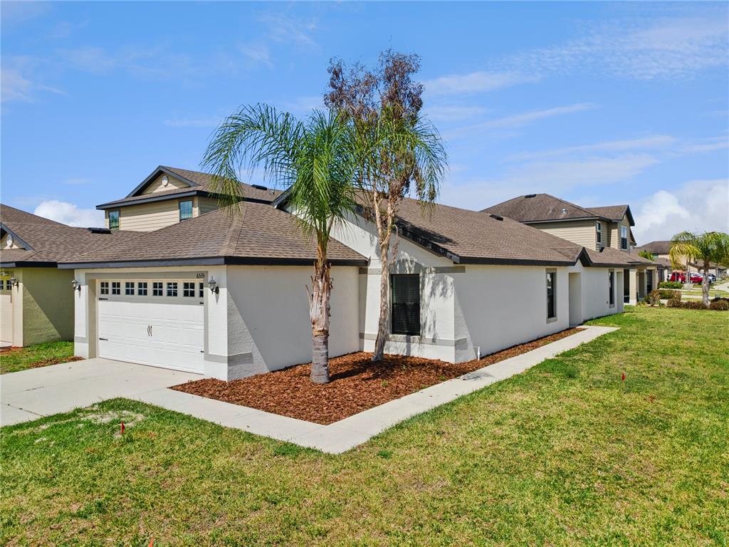 A single-story house with a white stucco exterior, a two-car garage, and a palm tree — 6535 BAIKAL PLACE, LAKELAND, FL