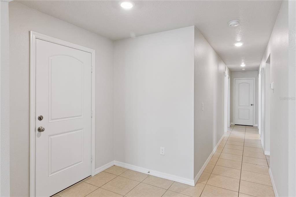 A bright entryway with tiled flooring leads to a long hallway with white doors — 6535 BAIKAL PLACE, LAKELAND, FL