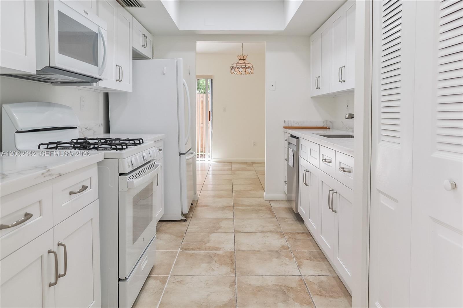 A white galley kitchen features tile flooring, white cabinetry, and stainless steel appliances — 11521 SW 109th Rd # 10A, Miami FL 33176, MIAMI, FL