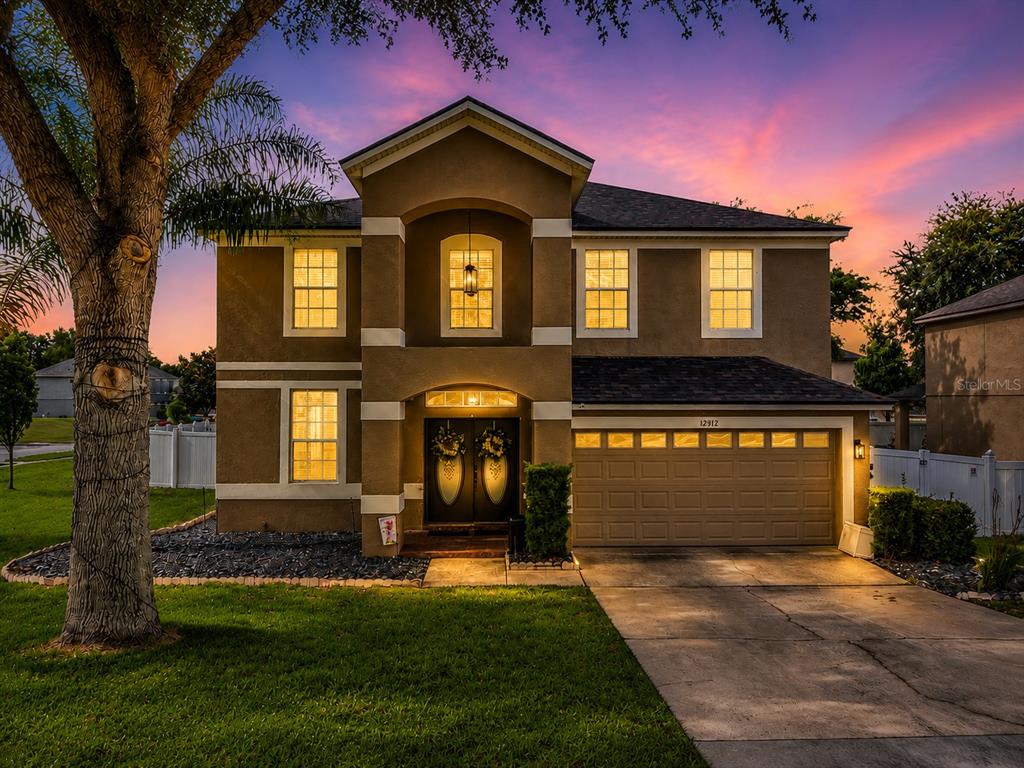 A two-story tan stucco house with a two-car garage at sunset — 12912 CLOVERDALE LANE, CLERMONT, FL