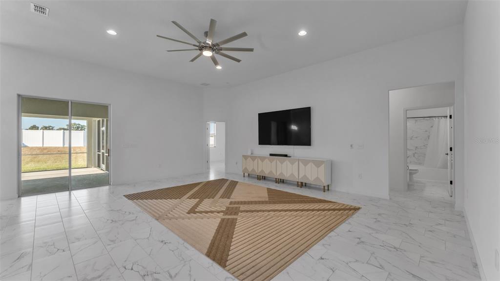 A spacious living room features white tile floors, a ceiling fan, and a large area rug — 1029 BERGAMOT DRIVE, BARTOW, FL