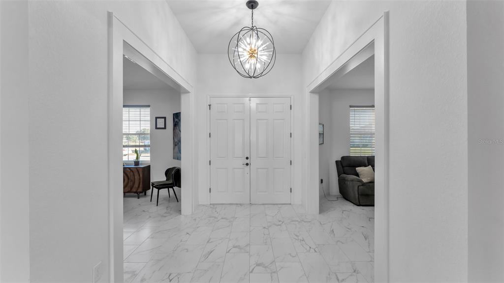 A bright foyer features white marble-look tile flooring, a modern chandelier, and double front doors — 1029 BERGAMOT DRIVE, BARTOW, FL